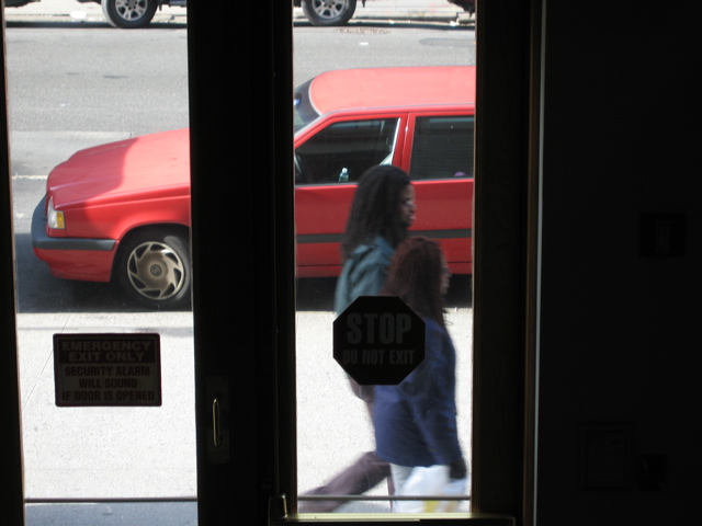 A white car pulls into the background parking space, as two people with long hair walk by