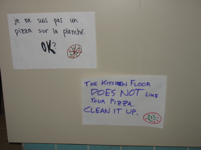 Two signs near the floor: "Je ne suis pas un pizza sur la planch&eacute;. OK?" "The kitchen floor DOES NOT like your pizza. Clean it up."