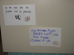 Two signs near the floor: "Je ne suis pas un pizza sur la planch&eacute;. OK?" "The kitchen floor DOES NOT like your pizza. Clean it up."