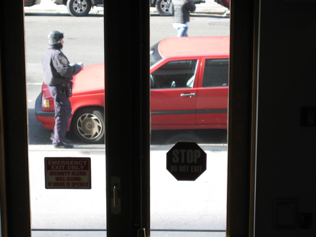 A policeman approaches the red car; A man jay-walks