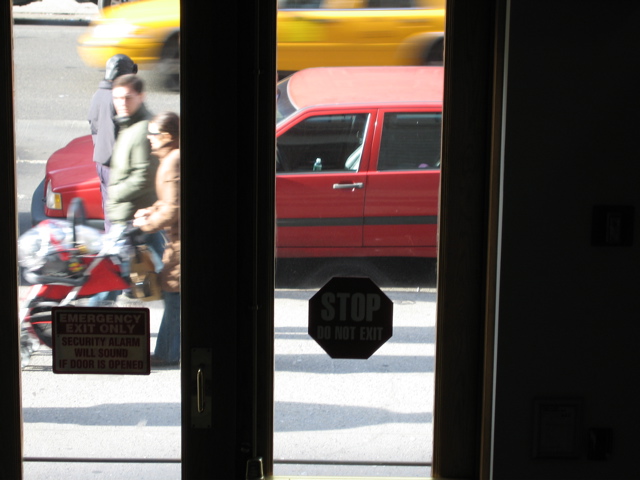 A couple with a stroller pass the policeman; A cab passes in the background