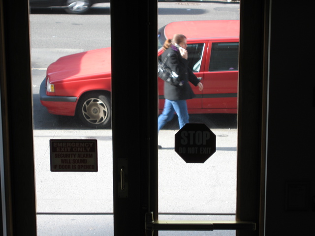 A woman with a purple scarf talks on her cell phone, as the SUV in the background has left its parking sopt