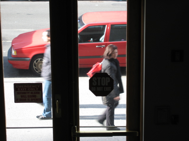A man passes a woman with a very bright red purse