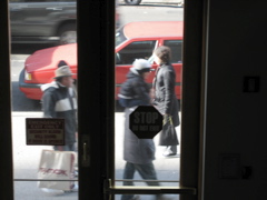A woman passes a man with a child on his shoulders and a man with a TJ Maxx bag; An SUV passes all