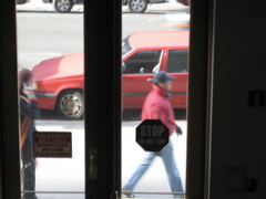 A woman on her cell phone behind a man in a red blazer; A car almost present going south