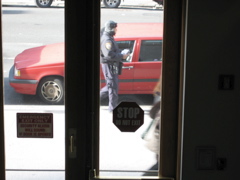 The policeman walks away, white book in hand; a woman walks past in the foreground