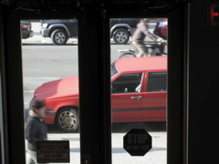 A man walks in the foreground, a man bikes in the background; The SUV in the background begins pulling out of its spot